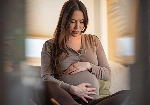 Beautiful pregnant woman sitting cross-legged and cradling her belly